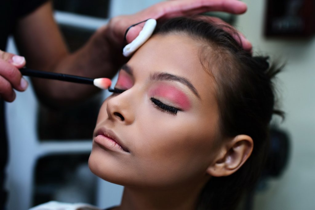 makeup artist applying red eye lashes over woman eye lids