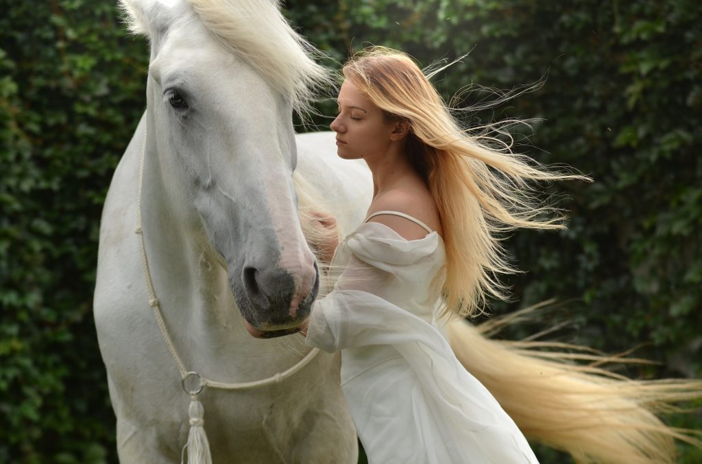 Beautiful woman wearing white top standing with white horse